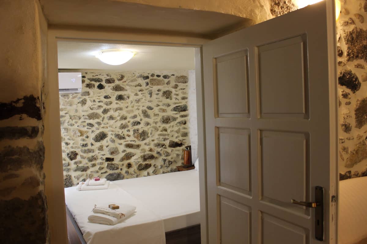 Ein Zimmer mit Steinwand, einem Bett mit weißer Bettwäsche und einer Tür mit Griff.