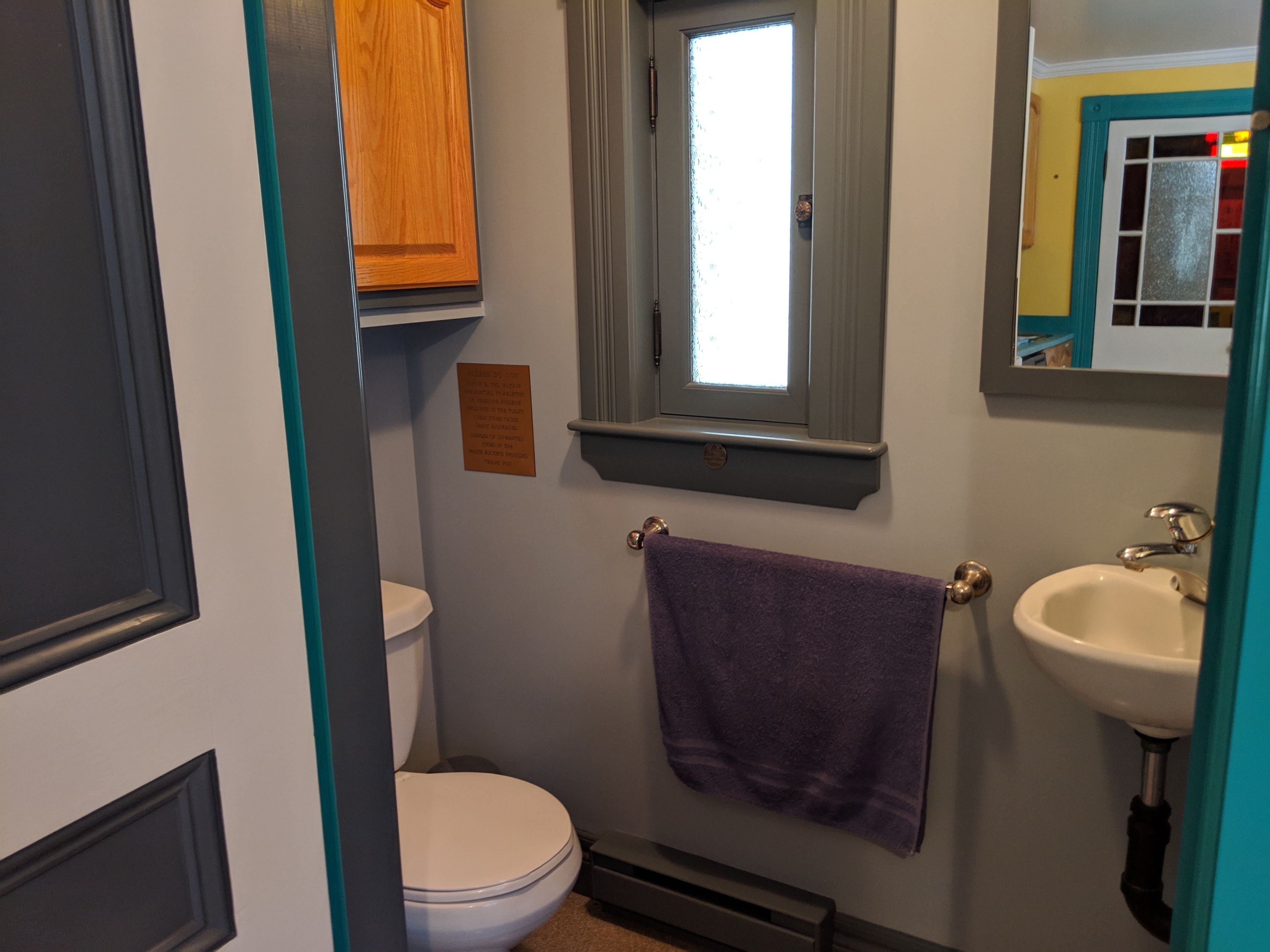 A bathroom with a toilet, a sink, a towel hanging on the wall, and a window.