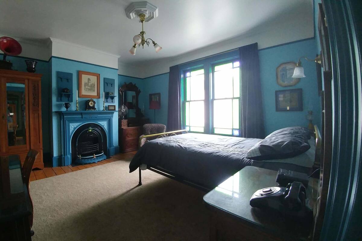 A bedroom with a bed, a dresser, a mirror, a fireplace, and a window with curtains.