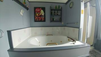 A bathroom with a large bathtub, a wall-mounted clock, and shelves with toiletries.