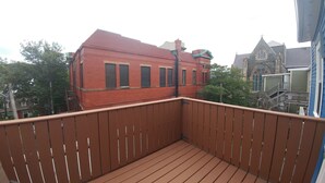 A wooden balcony with a view of a red brick building and a church with a pointed roof. - Gower Manor Historical Bed & Breakfast (St. John's)