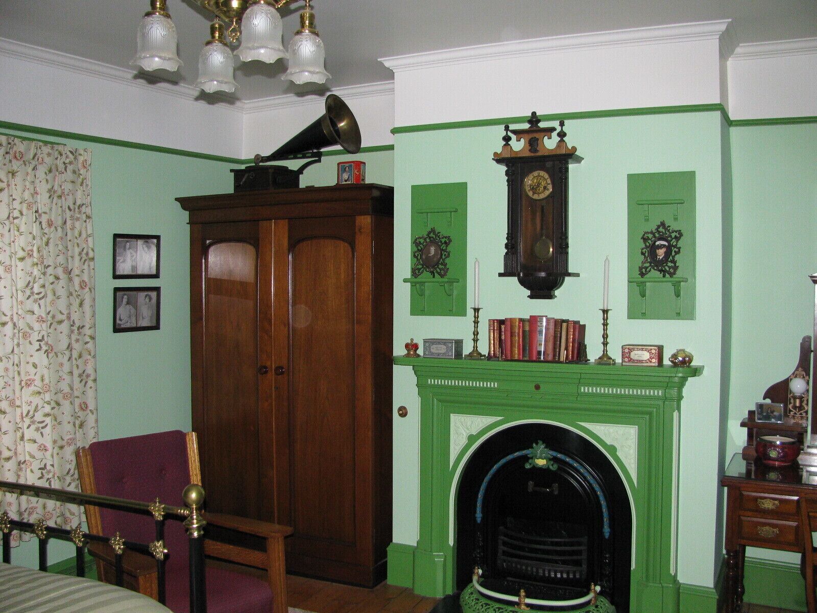 A room with a green fireplace, a wooden cabinet, and a bed with a floral curtain.