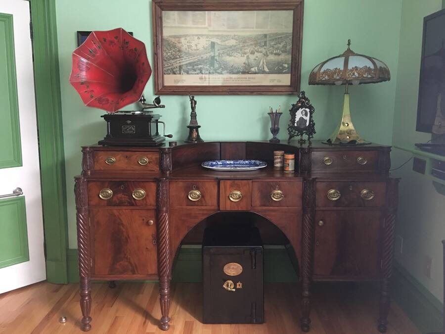 A vintage wooden desk with multiple drawers, a phonograph, a framed historical map, and a lamp.