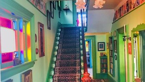 A staircase with patterned carpet leading to a landing, surrounded by walls with framed pictures and a chandelier. - Gower Manor Historical Bed & Breakfast (St. John's)