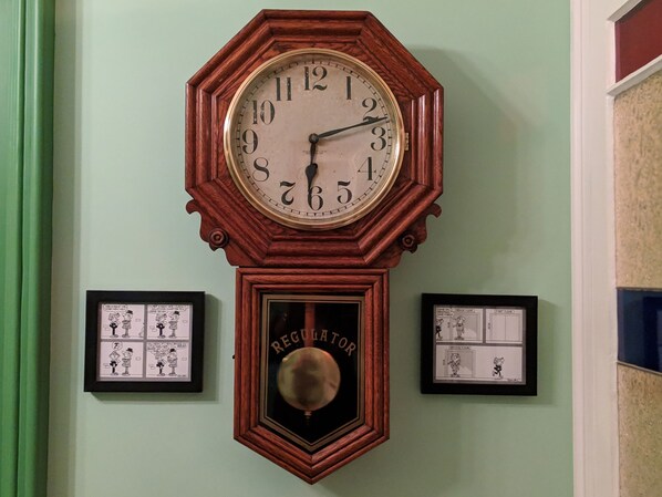 A wall-mounted grandfather clock with a pendulum, surrounded by framed comic strips. - Gower Manor Historical Bed & Breakfast (St. John's)