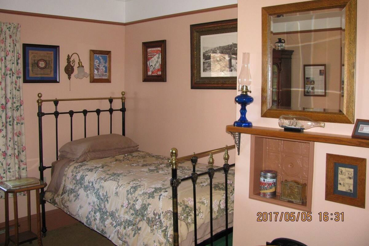 A bedroom with a four-poster bed, a wooden nightstand, a mirror, and various framed pictures on the walls.