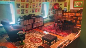A cozy living room with a fireplace, a bookshelf, a dining table, and a variety of posters on the walls. - Gower Manor Historical Bed & Breakfast (St. John's)