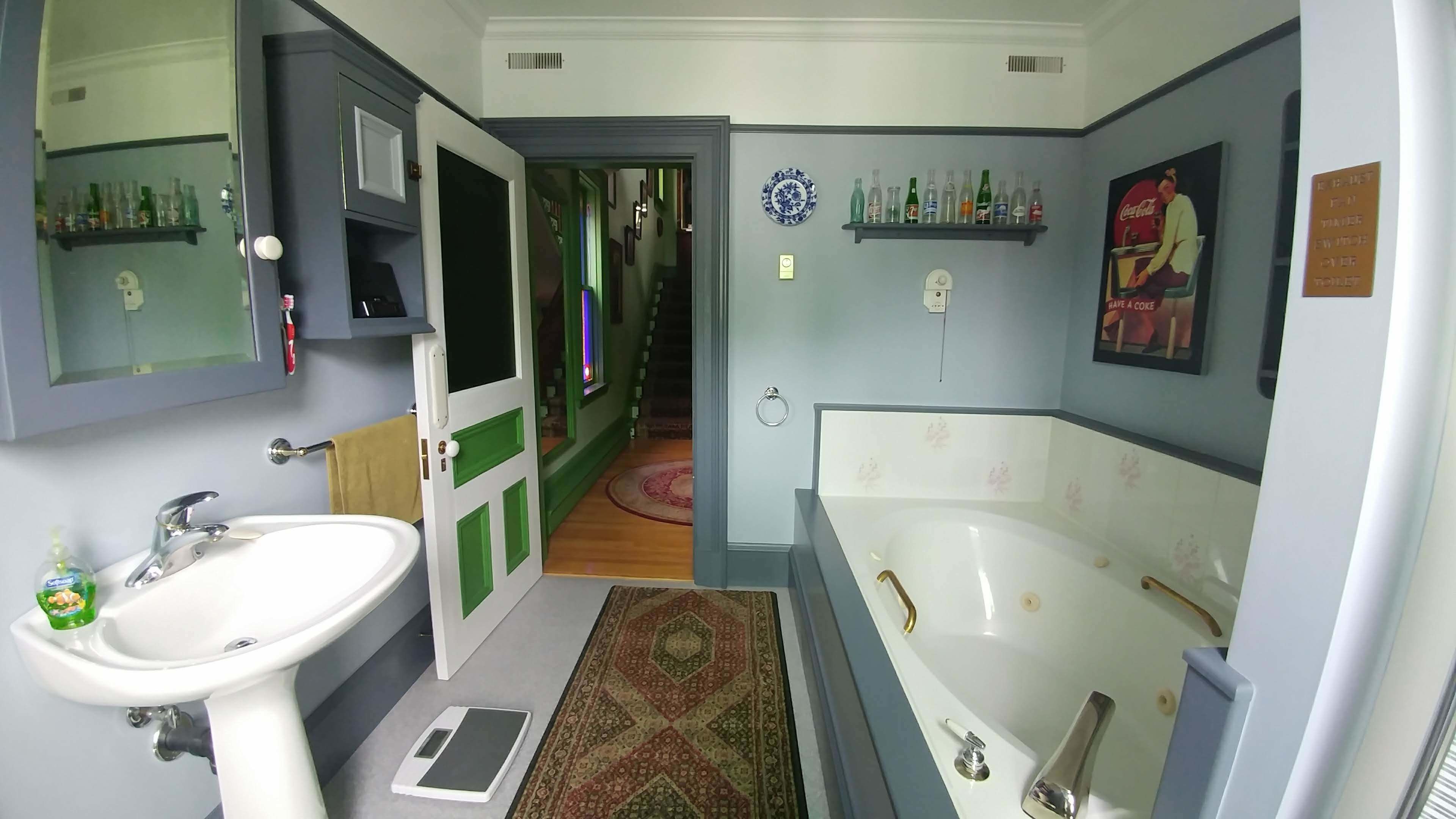 A bathroom with a sink, mirror, green door, shower, and shelves with toiletries.