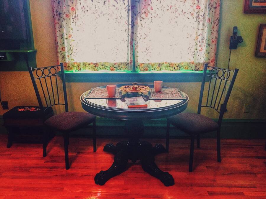 A dining table with chairs, a window with floral curtains, and a telephone on the wall.