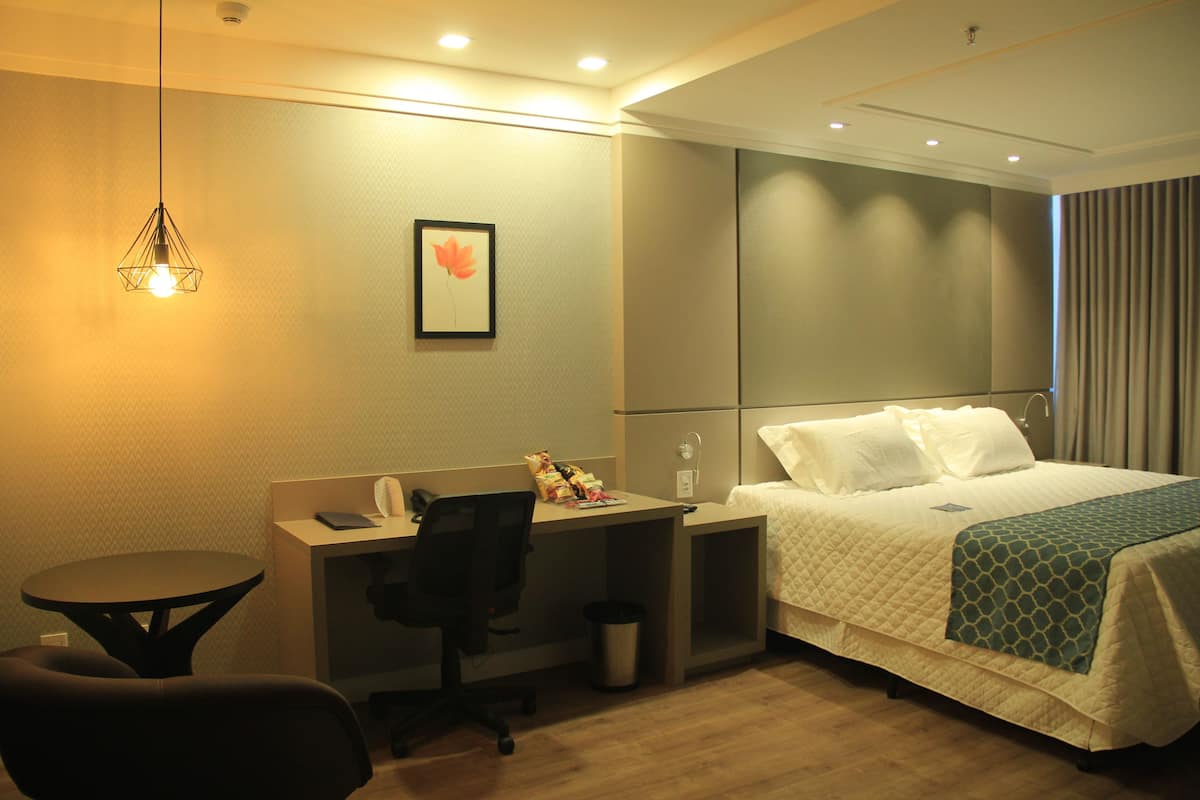 A hotel room with a bed, desk, chair, and a small table.
