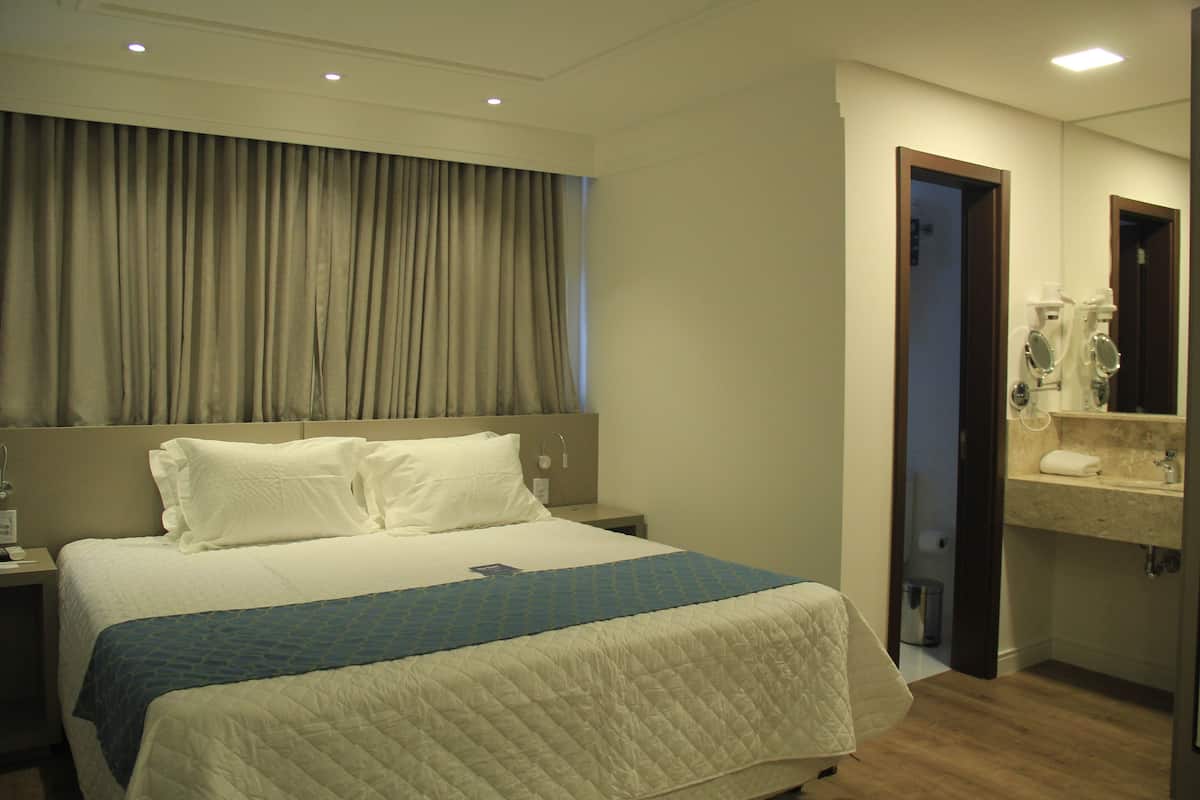 A hotel room with a large bed, a nightstand, a bathroom with a mirror and sink, and a curtain covering the window.