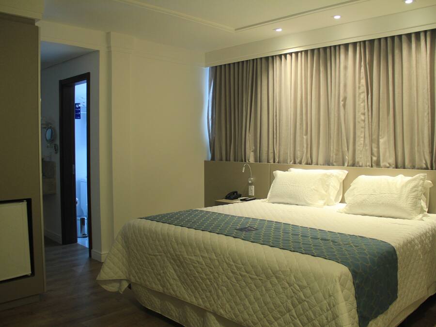 Een hotelkamer met een groot bed, een nachtkastje met een lamp en een gordijn voor het raam.