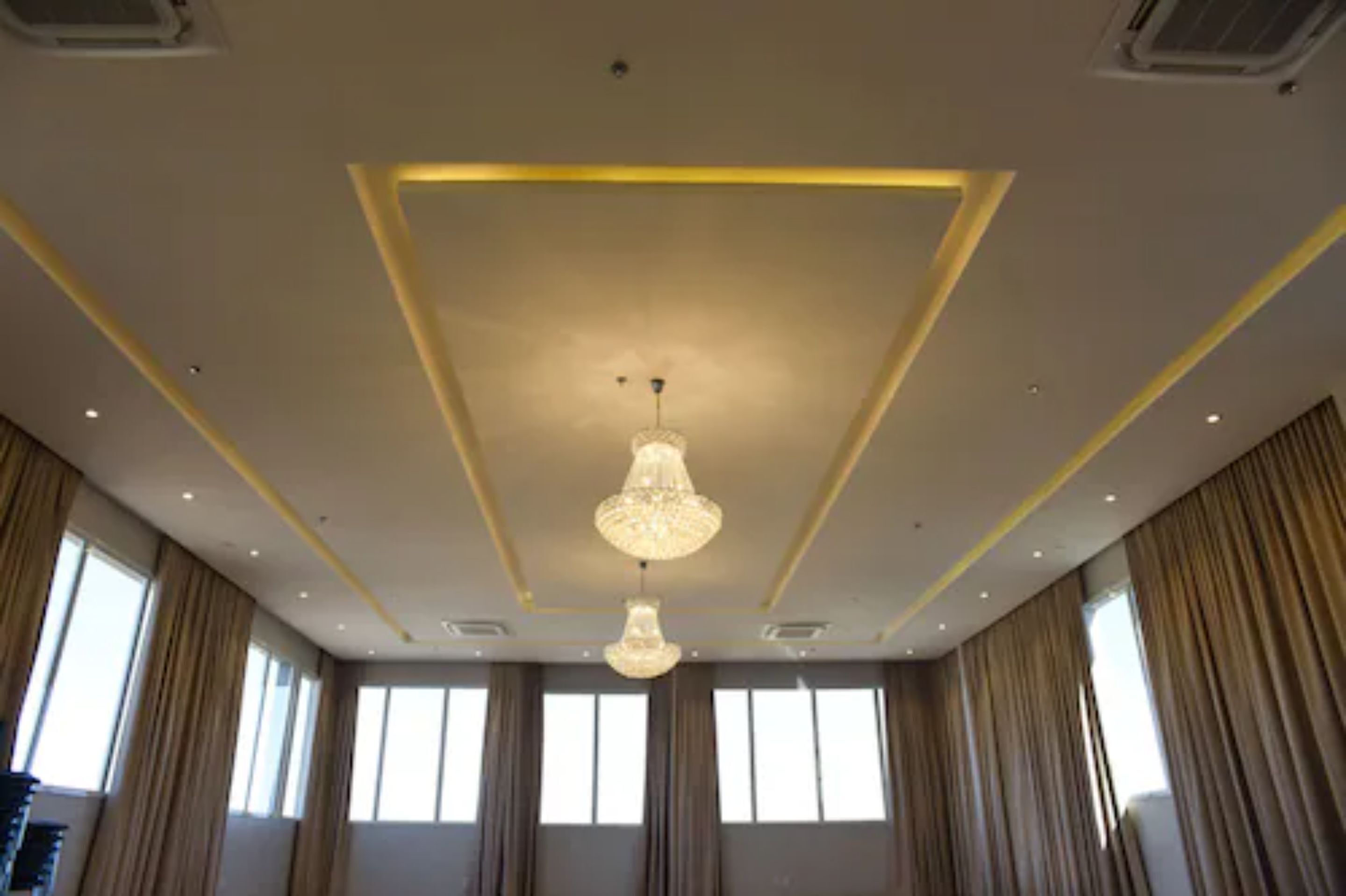 Una habitación de hotel con un diseño moderno en el techo, ventanas amplias y un candelabro.