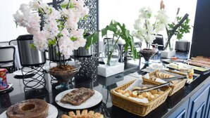 A buffet with various food items, including pastries and bread, and decorative white flowers. - Blue Open Hotel (Erechim)