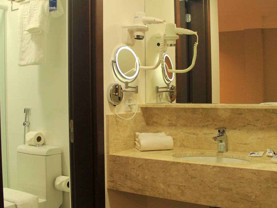 Un baño con lavamanos de mármol, un espejo con luz de aro, un perchero para toallas y un inodoro.