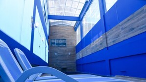 A modern, enclosed swimming area with blue walls and a wooden floor, featuring a single white sun lounger. - Blue Open Hotel (Erechim)