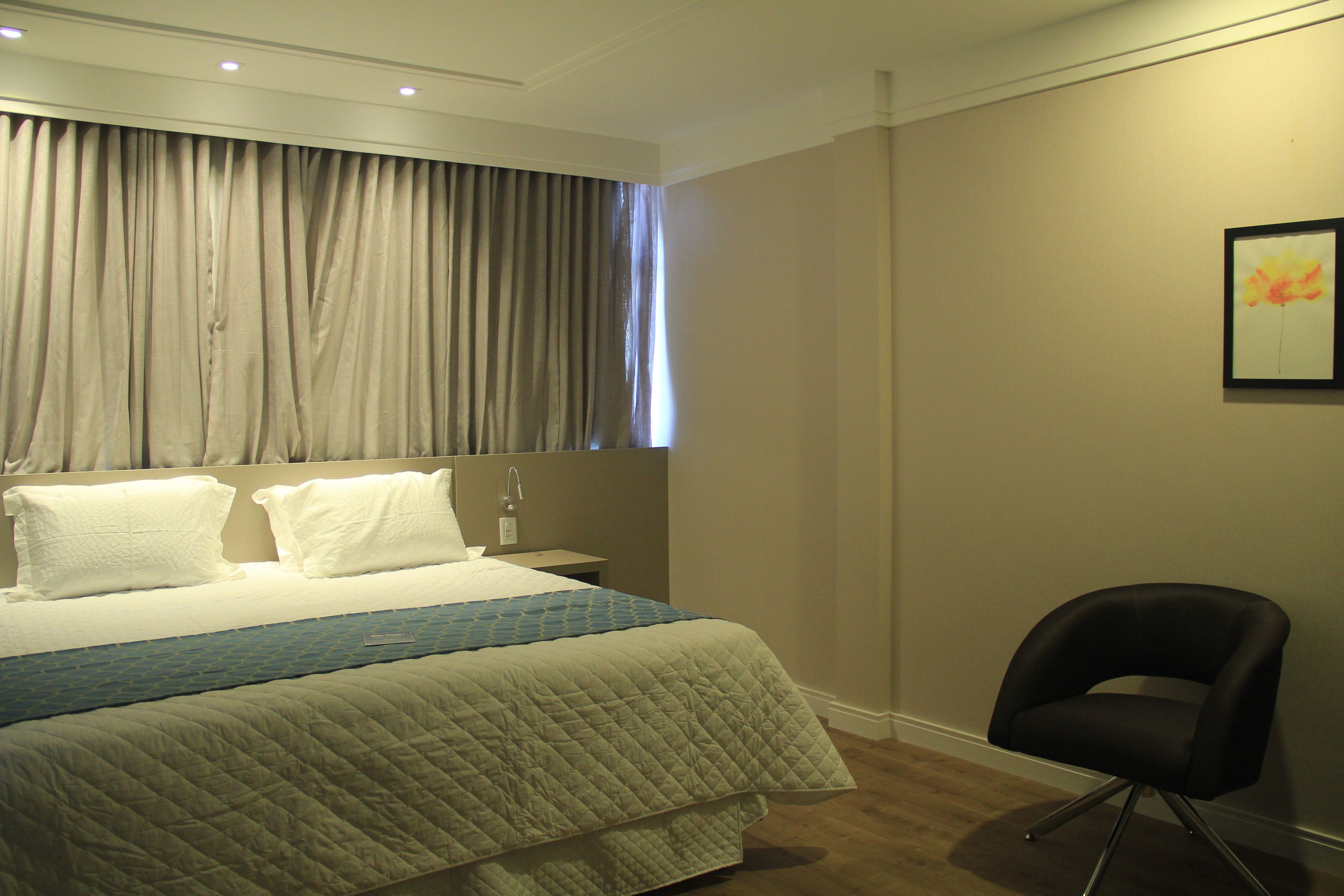 A hotel room with a large bed, a nightstand, a chair, and a window with curtains.