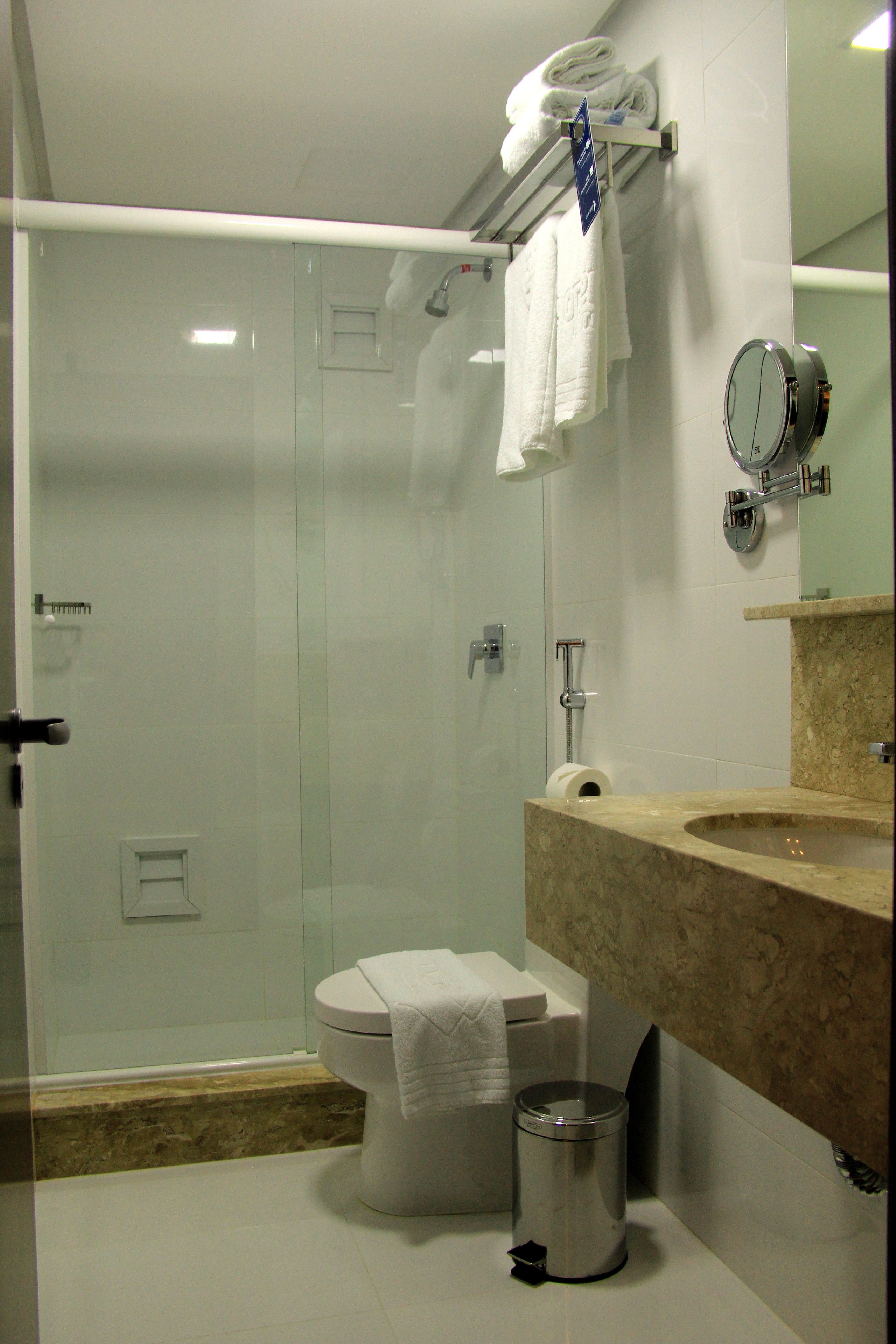 Un baño moderno con cabina de ducha de vidrio, inodoro, lavabo con encimera de mármol y espejo.