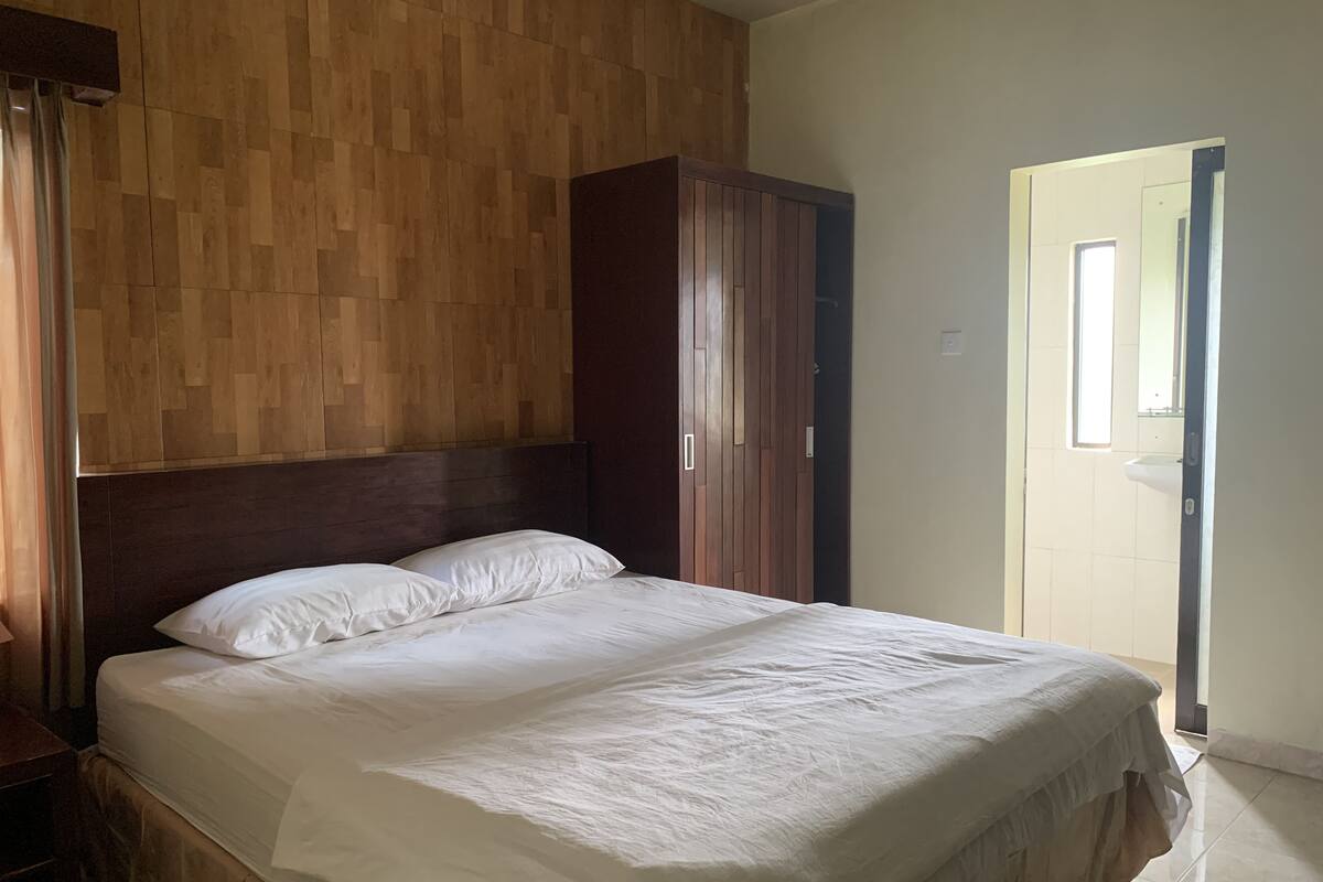 A bedroom with a wooden headboard, a large bed with white bedding, and a wardrobe.