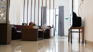 A modern reception area with a polished floor, a reception desk, a seating area with patterned cushions, vertical wooden slats, and a ceiling light fixture. - Cukoo House (Hanoi)