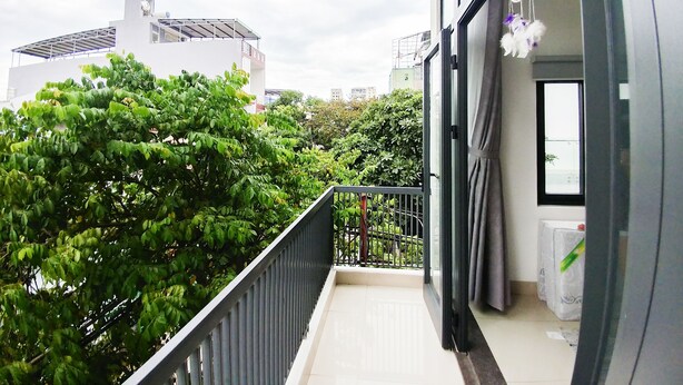 A balcony with a view of a cityscape, a window with a curtain, and a small table with a plant. - Cukoo House (Hanoi)