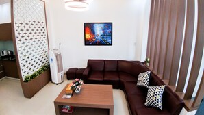 A modern living room with a brown sectional sofa, a wooden coffee table, and a painting on the wall. - Cukoo House (Hanoi)