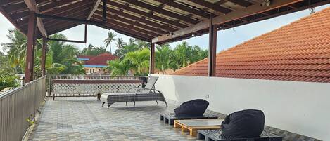 A covered outdoor area with tiled flooring, metal benches, and a view of a building with a red roof.