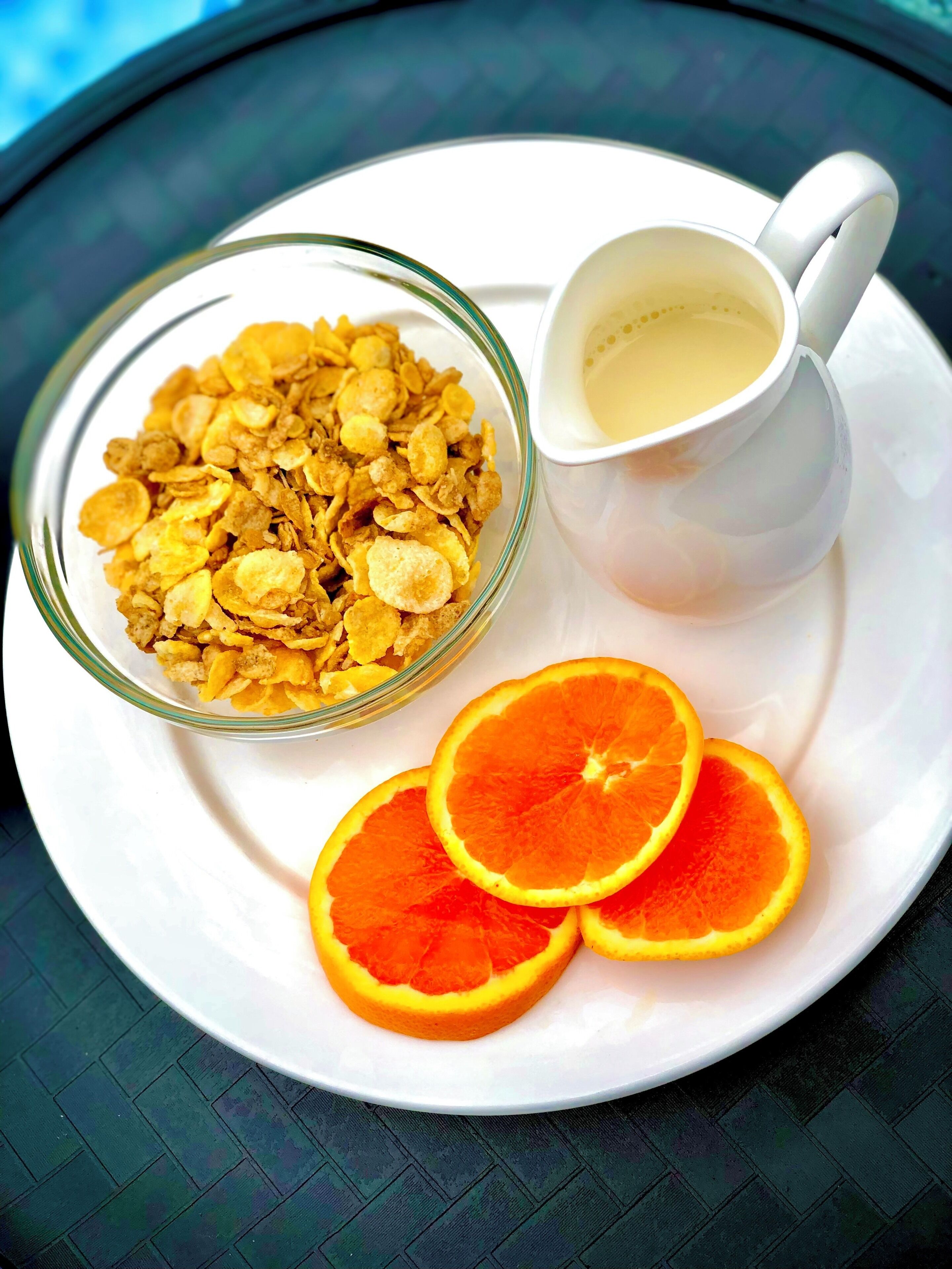 A glass bowl of cereal, a white cup with a beverage, and orange slices on a white plate.