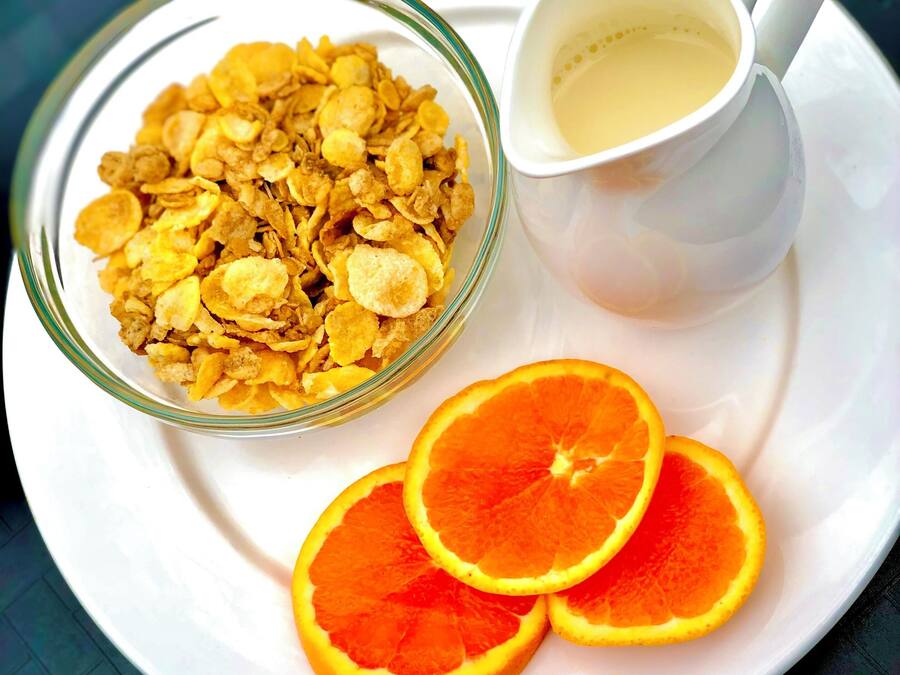 A glass bowl of cereal, a white cup with a beverage, and orange slices on a white plate.