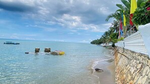 A coastal beach scene with clear skies, calm waters, and a stone wall with a flag. - Marick Beach Resort (Carmen)