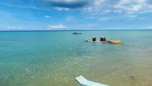 A clear turquoise sea with a boat anchored near a stone structure. - Marick Beach Resort (Carmen)