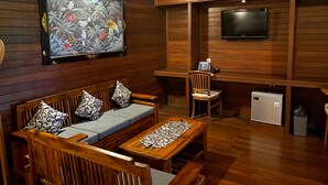 Un interior de madera con un sofá, sillas, una mesa, un televisor y un refrigerador pequeño.