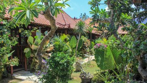 Un jardín exuberante con diversas plantas tropicales y un edificio tradicional con techo de tejas.