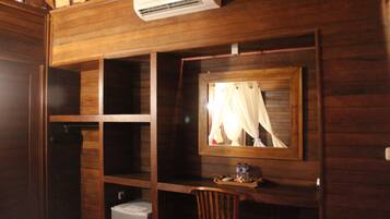 Une pièce en bois avec un bureau, une chaise et un miroir. Il y a un climatiseur au-dessus du bureau et un petit réfrigérateur en dessous.