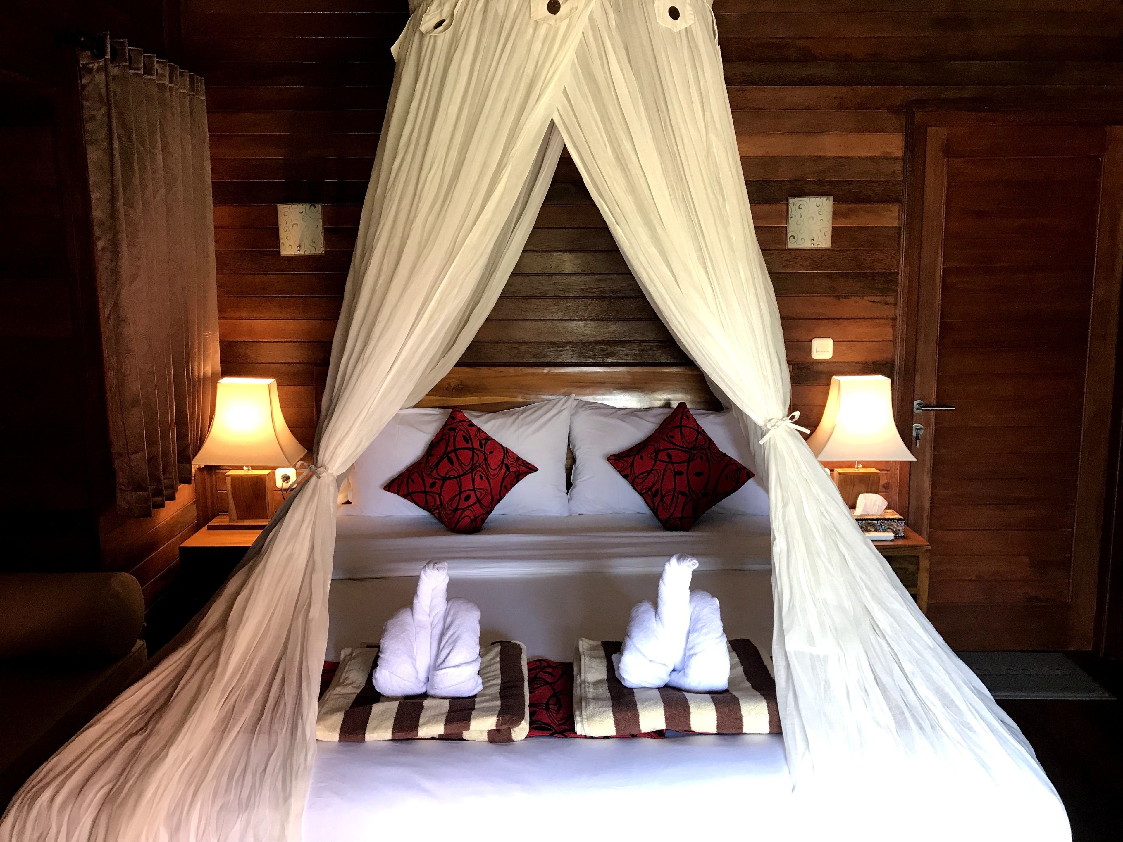 A bed with a canopy, two pillows, a bedside table with a lamp, and a wooden wall.