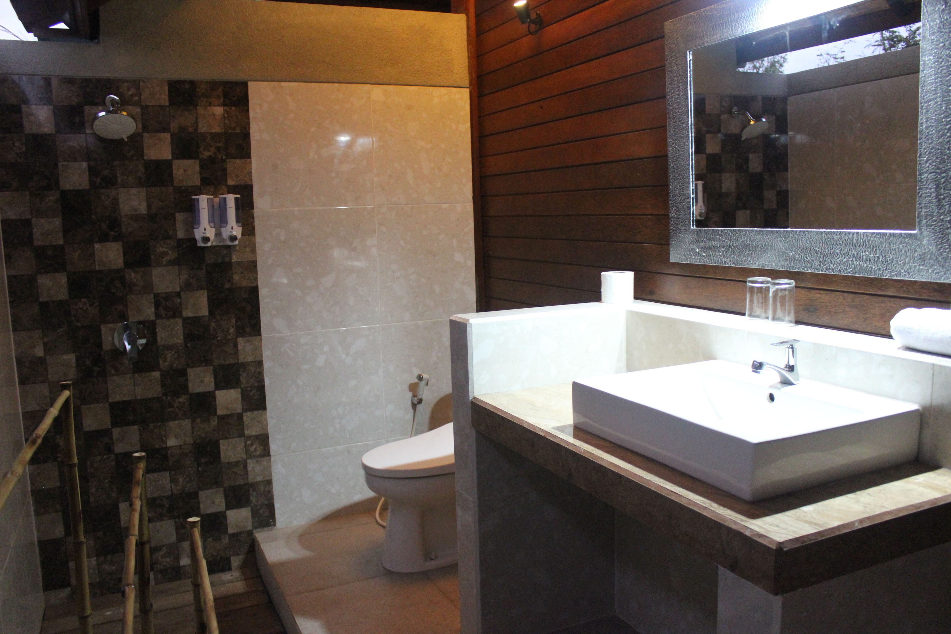 Un bagno con parete rivestita di piastrelle a scacchi, un water, un lavandino con specchio e zona doccia.