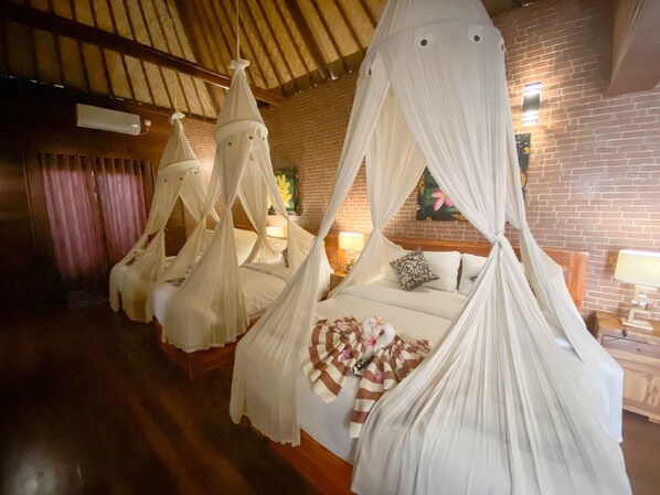 Une chambre dotée de quatre lits à baldaquin, chacun surmonté d’un ciel de lit blanc et recouvert d’une couverture à rayures. La chambre a un plancher en bois et des murs en briques.