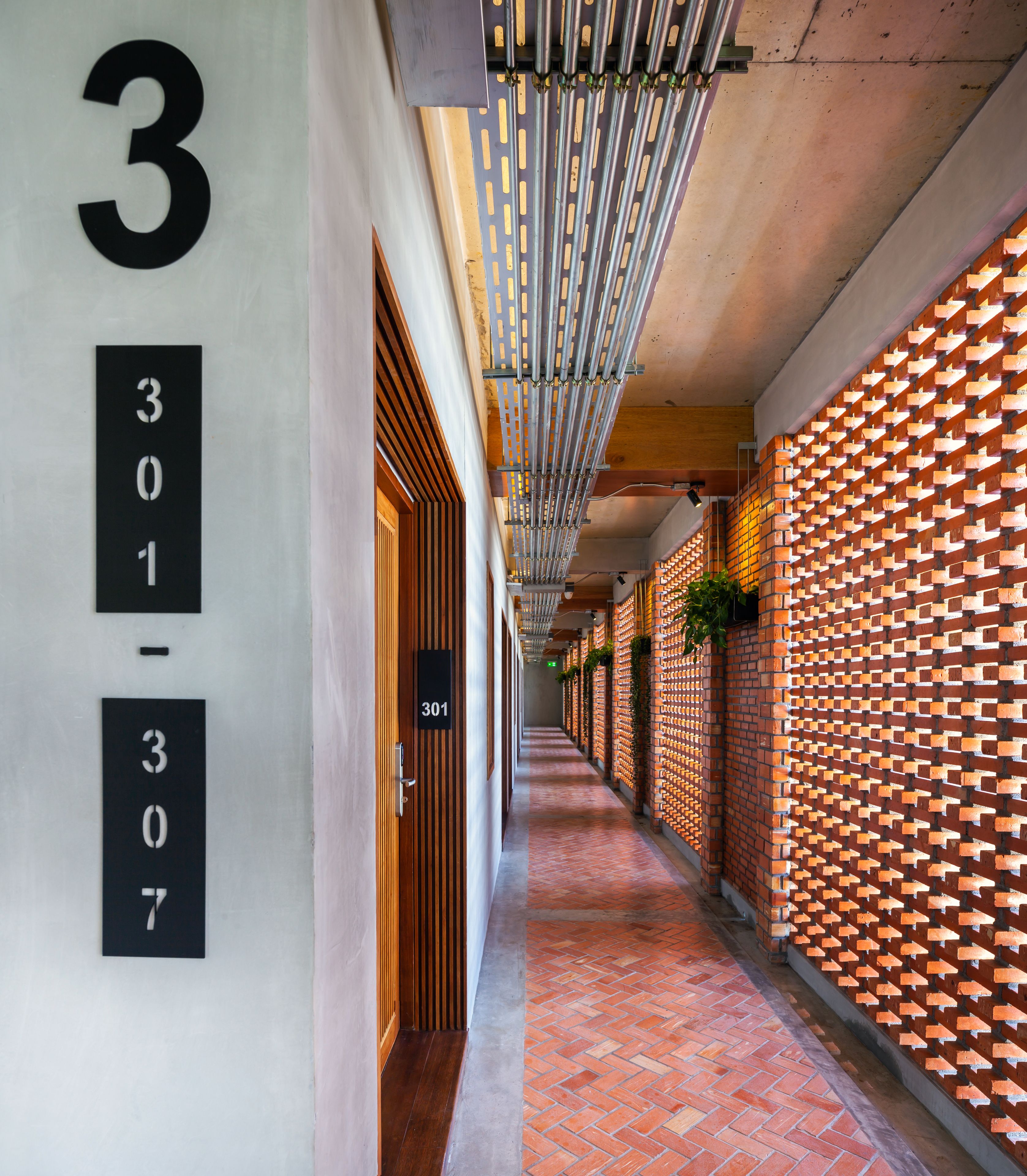 A hallway with a brick wall on one side and a white wall on the other, featuring a number sign with '301-307' and a door with a handle.
