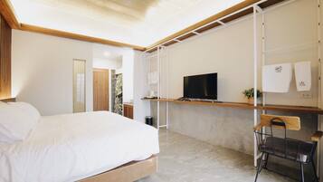 Une chambre moderne avec un grand lit, un téléviseur posé sur une étagère, une chaise et une petite table.