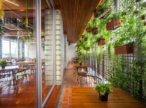 Un espace intérieur moderne doté d’un plancher en bois, de cloisons en verre et d’une variété de plantes vertes disposées dans des jardinières suspendues et des bacs fixés au mur.