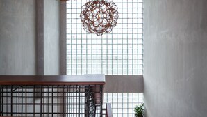 Una escalera con barandilla de madera y pasamanos de metal, que conduce a una habitación con ventanas amplias y lámparas de mimbre colgantes.
