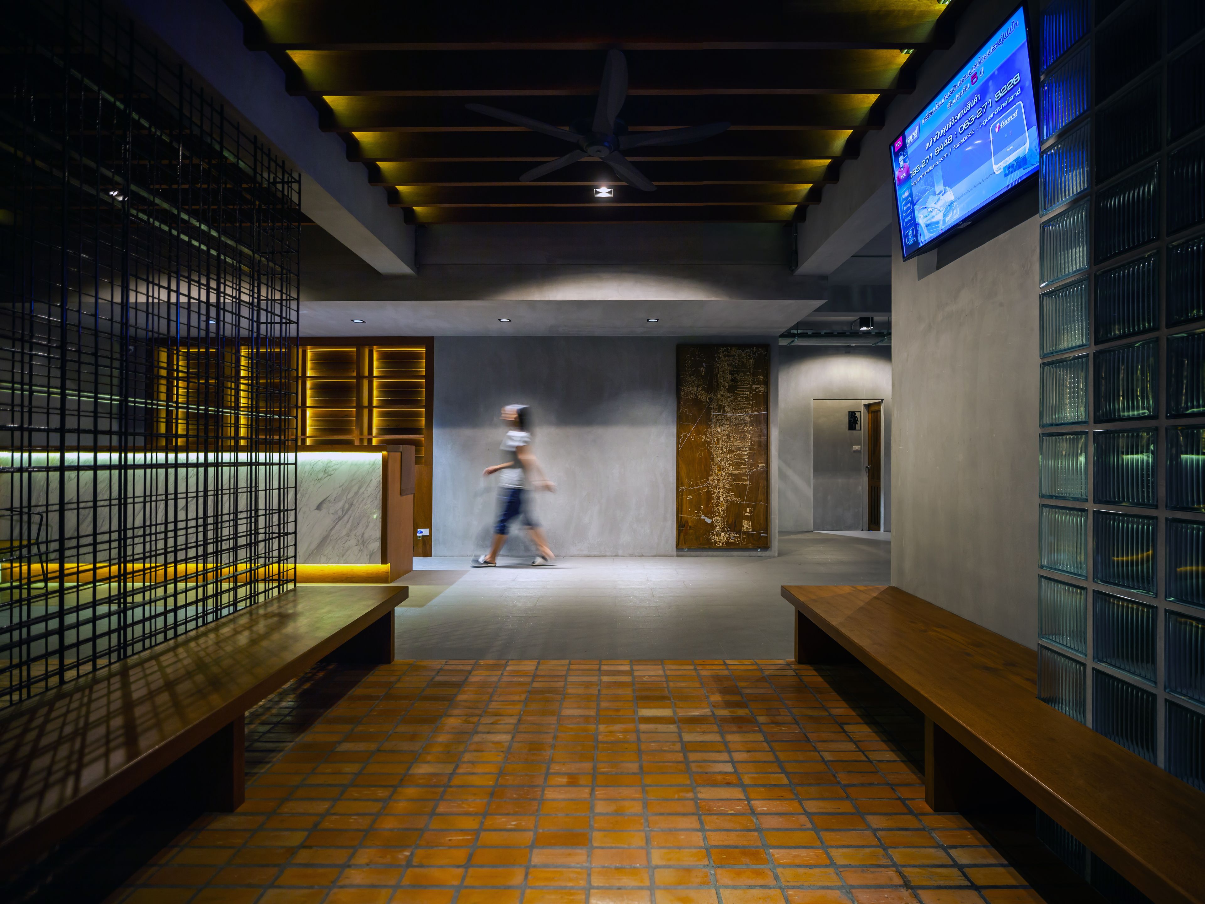 A modern interior with a tiled floor, wooden benches, a reception desk, and a digital display.