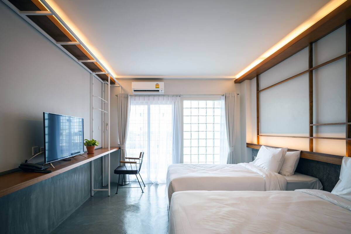 Habitación de hotel con dos camas, televisión, escritorio y ventana con cortinas.