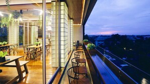 Un interior moderno con comedor, un balcón con plantas y vista a la ciudad al anochecer.