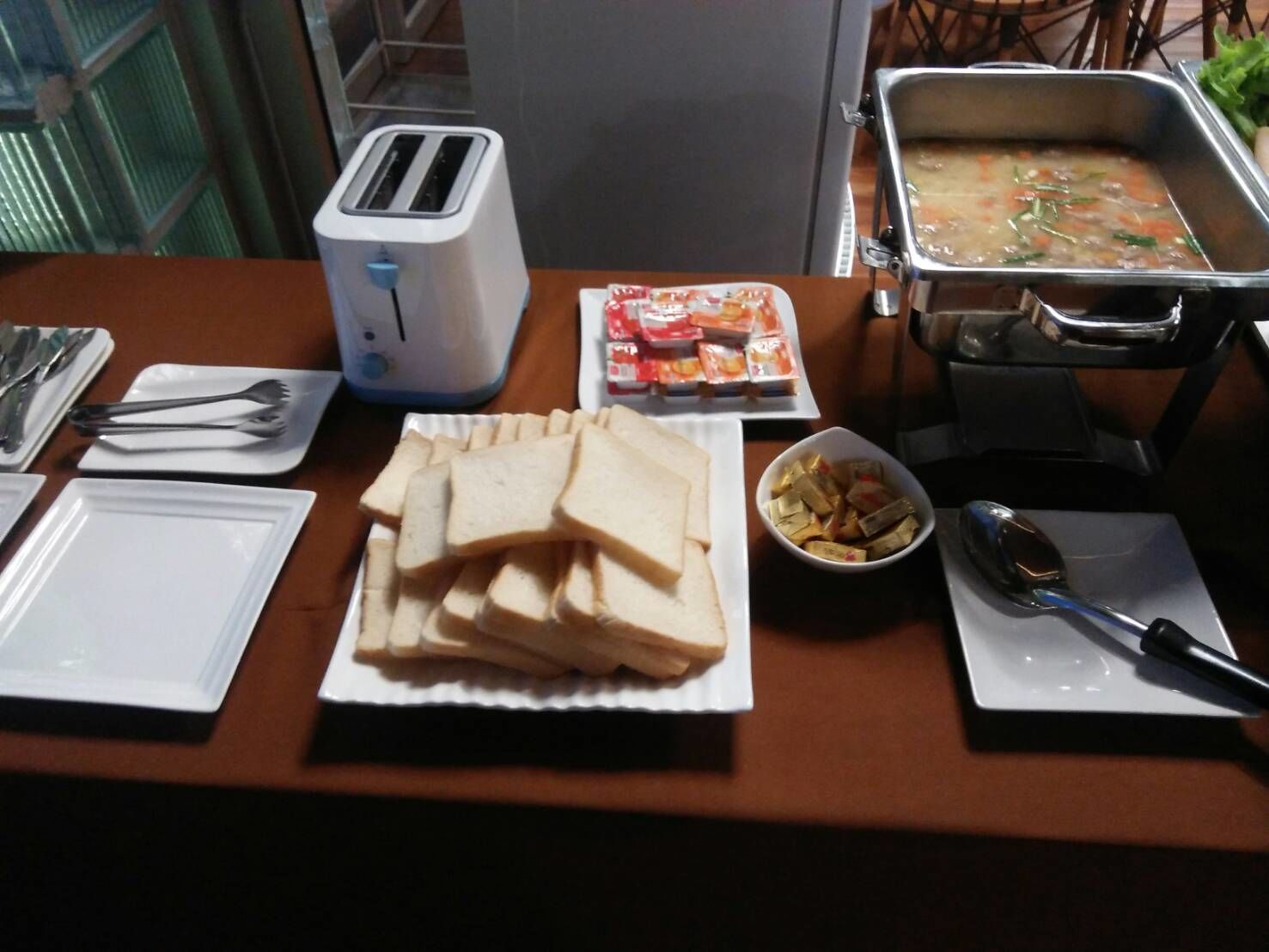A breakfast setup with a toaster, bread, condiments, a bowl of fruit, and a soup container.