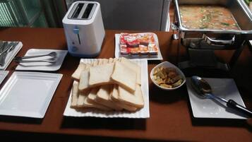 A breakfast setup with a toaster, bread, condiments, a bowl of fruit, and a soup container.