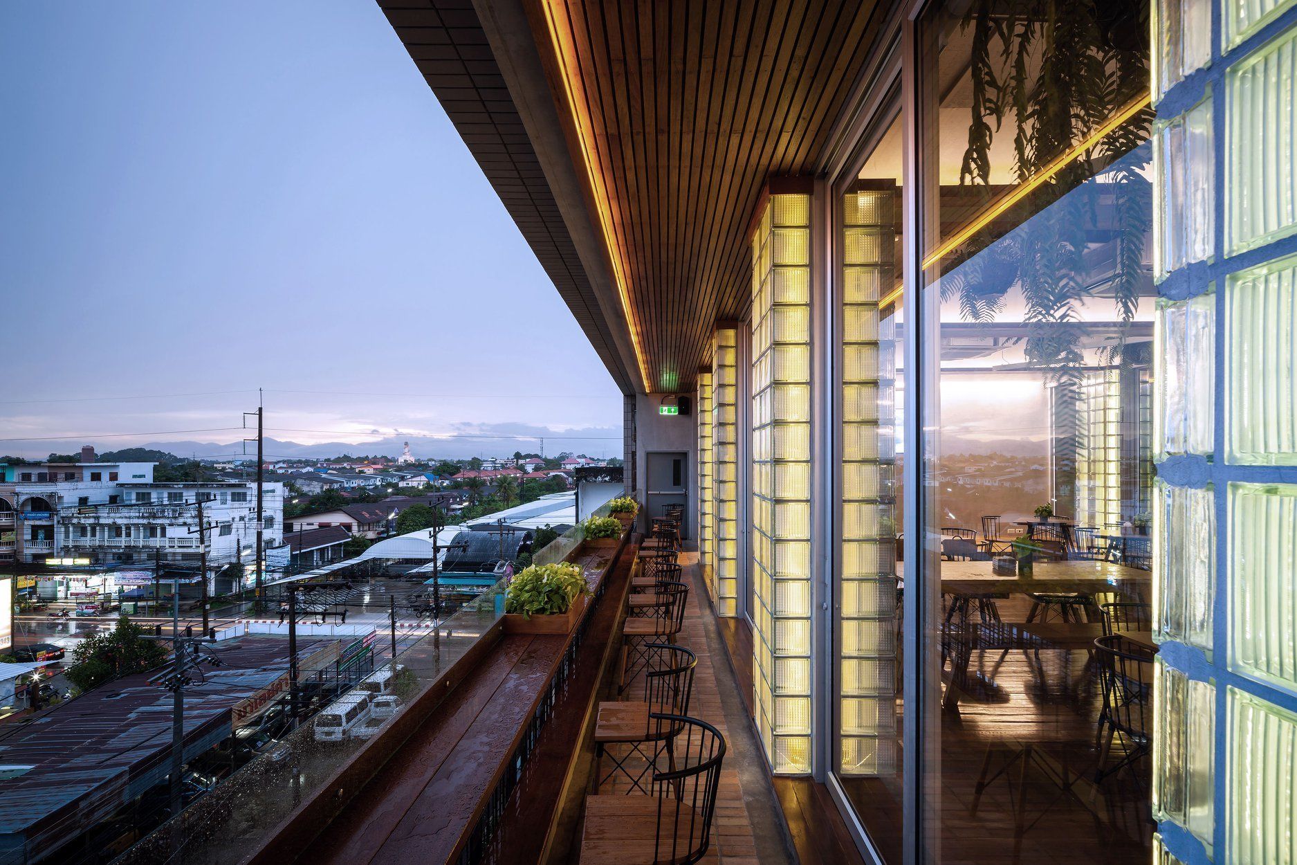 A restaurant with a view of a cityscape, featuring a long counter with chairs and a wooden ceiling.