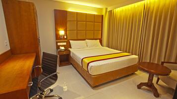 A hotel room with a bed, a desk, a chair, a nightstand, and a lamp.