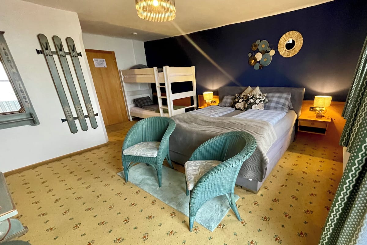 Une chambre avec un lit superposé, deux fauteuils en osier, une moquette à motifs et un mur décoré d’assiettes.