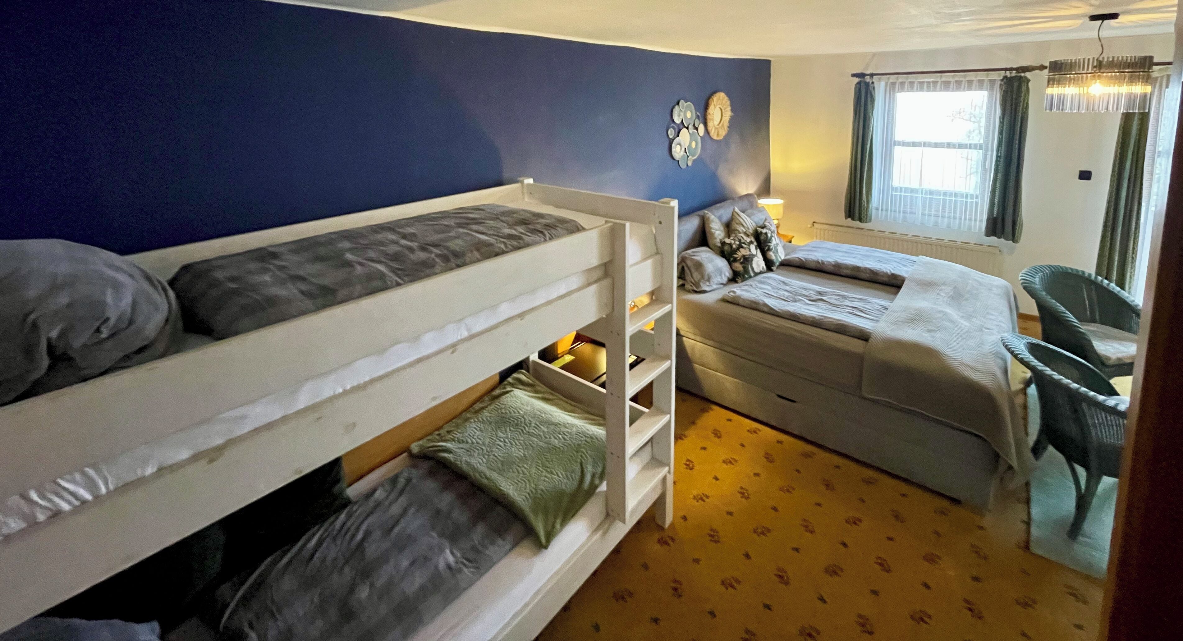 A room with two bunk beds, a desk, a chair, and a window with curtains.